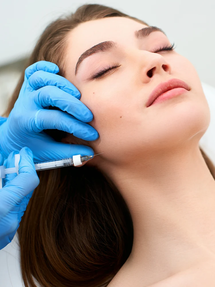 Medical professional administering Radiesse dermal filler injection to female patient's jawline area in sterile treatment room.